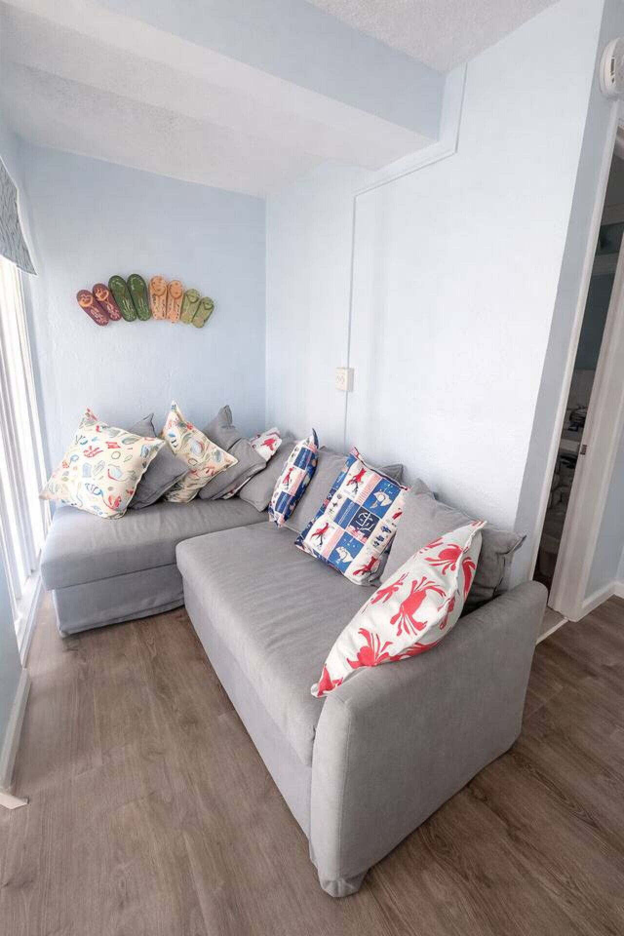 A modern living room with a grey sectional sofa, patterned cushions, and a wall-mounted shoe rack.