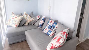 A modern living room with a grey sectional sofa, patterned cushions, and a wall-mounted shoe rack.