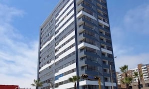 Un immeuble à plusieurs étages doté de balcons, un ciel dégagé et des palmiers.