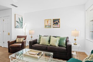 A living room with a brown leather sofa, a glass coffee table, and two wall-mounted lamps. - Renovated 1-bedroom condo in lovely Orange Beach (Orange Beach)