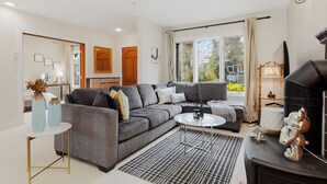 Uma sala de estar moderna com um sofá modular cinza, uma mesinha de centro redonda e um tapete preto e branco.