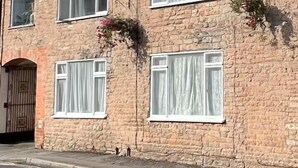 Una casa de maó de dues plantes amb nombroses finestres, una xemenea i una entrada tancada per una reixa.