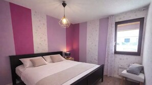 Ein Schlafzimmer mit Bett, Nachttisch, Lampe, Fenster und einem Sessel.