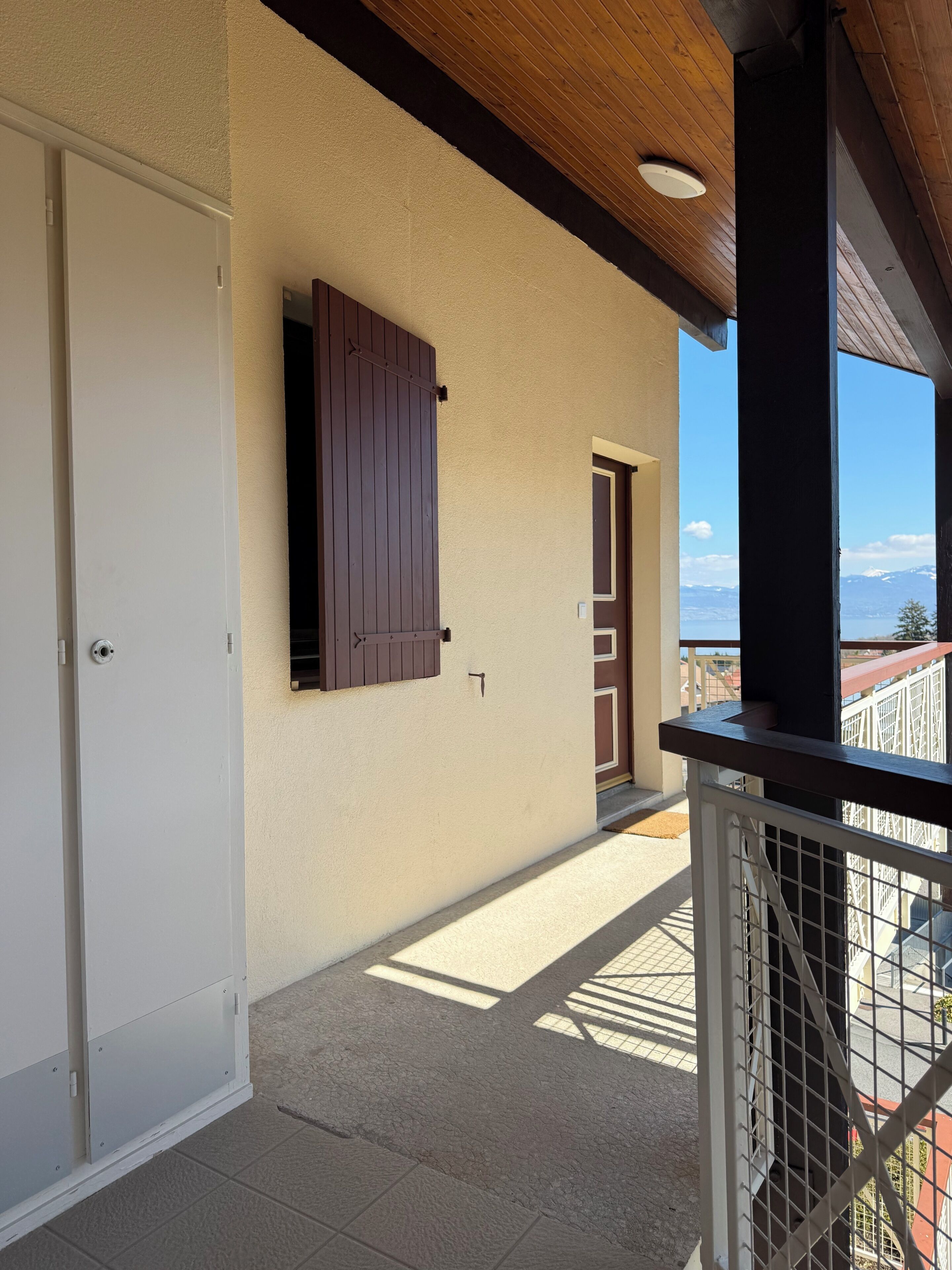 Un balcón con vistas a las montañas, una puerta blanca y un cerrojo marrón en la pared.