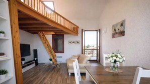 Ein geräumiger Wohnbereich mit einer Holztreppe, einer Couch, einem Esstisch mit Stühlen und einem Balkon mit Blick.
