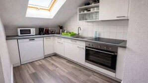 Eine kleine Küche mit weißen Schränken, einer Mikrowelle, einem Geschirrspüler, einer Spüle und einem Backofen.