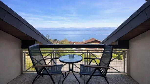 Ein Balkon mit Tisch und Stühlen mit Blick auf ein Gewässer und die Ferne.