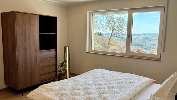 Une chambre avec un grand lit, une armoire, une fenêtre donnant sur un beau paysage et un luminaire au plafond.
