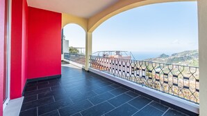 Un balcone con vista sul mare e sulle colline, un muro rosso e un pavimento piastrellato.