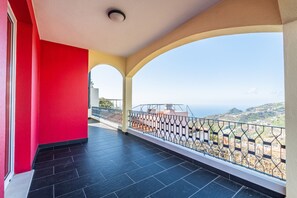 A balcony with a view of the sea and hills, a red wall, and a tiled floor. - Villa Vineyard by Homie (Câmara de Lobos)