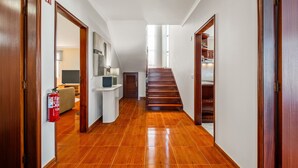 Un corridoio con pavimento in legno, un estintore, una scala e una porta che dà su una stanza con un letto.