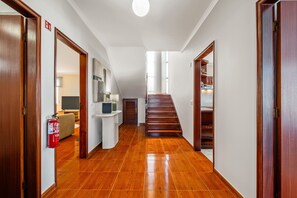 A hallway with wooden flooring, a fire extinguisher, a staircase, and a door leading to a room with a bed. - Villa Vineyard by Homie (Câmara de Lobos)