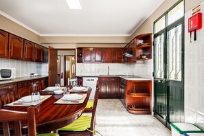 A kitchen with wooden cabinets, a dining table set with plates and glasses, a microwave, and a dishwasher. - Villa Vineyard by Homie (Câmara de Lobos)