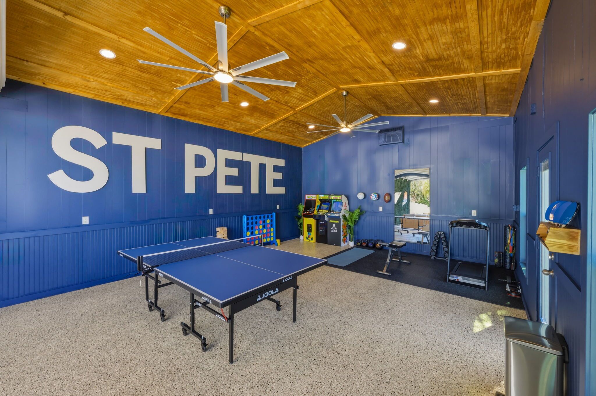 Una habitación con mesa de ping pong, equipo de ejercicio y un cartel grande que dice 'ST PETE'.