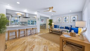 A modern living room with a sofa, coffee table, and a dining area with bar stools. - NEW - Sweet St Pete - 5 Minutes to beach - Heated Pool, Hot Tub, Sauna, + more (St. Petersburg)