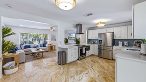 A modern kitchen with white cabinets, stainless steel appliances, and a marble floor. - NEW - Sweet St Pete - 5 Minutes to beach - Heated Pool, Hot Tub, Sauna, + more (St. Petersburg)