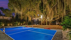 An outdoor tennis court with a net, surrounded by trees and string lights. - Boho Villa by Glam Homes (Miami)