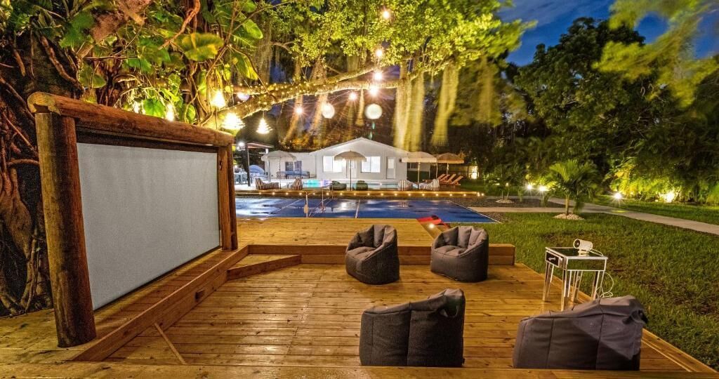 An outdoor deck with a wooden floor, bean bag chairs, a projector screen, and a pool.