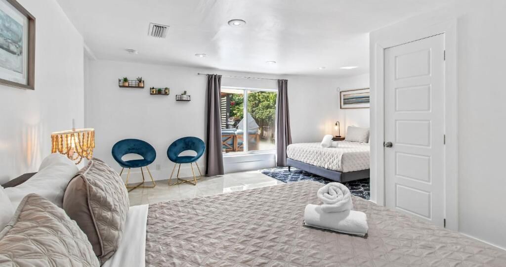 Une chambre moderne comprenant un lit, deux chaises, une table de chevet, une lampe et une porte donnant sur un balcon.