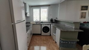 Eine kleine Küche mit Waschmaschine, Spüle und einem Fenster mit Jalousien.