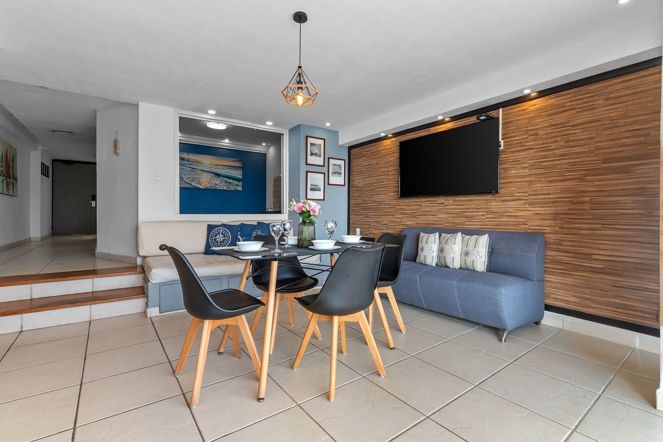 A modern living room with a dining area, a blue sofa, and a mounted TV.
