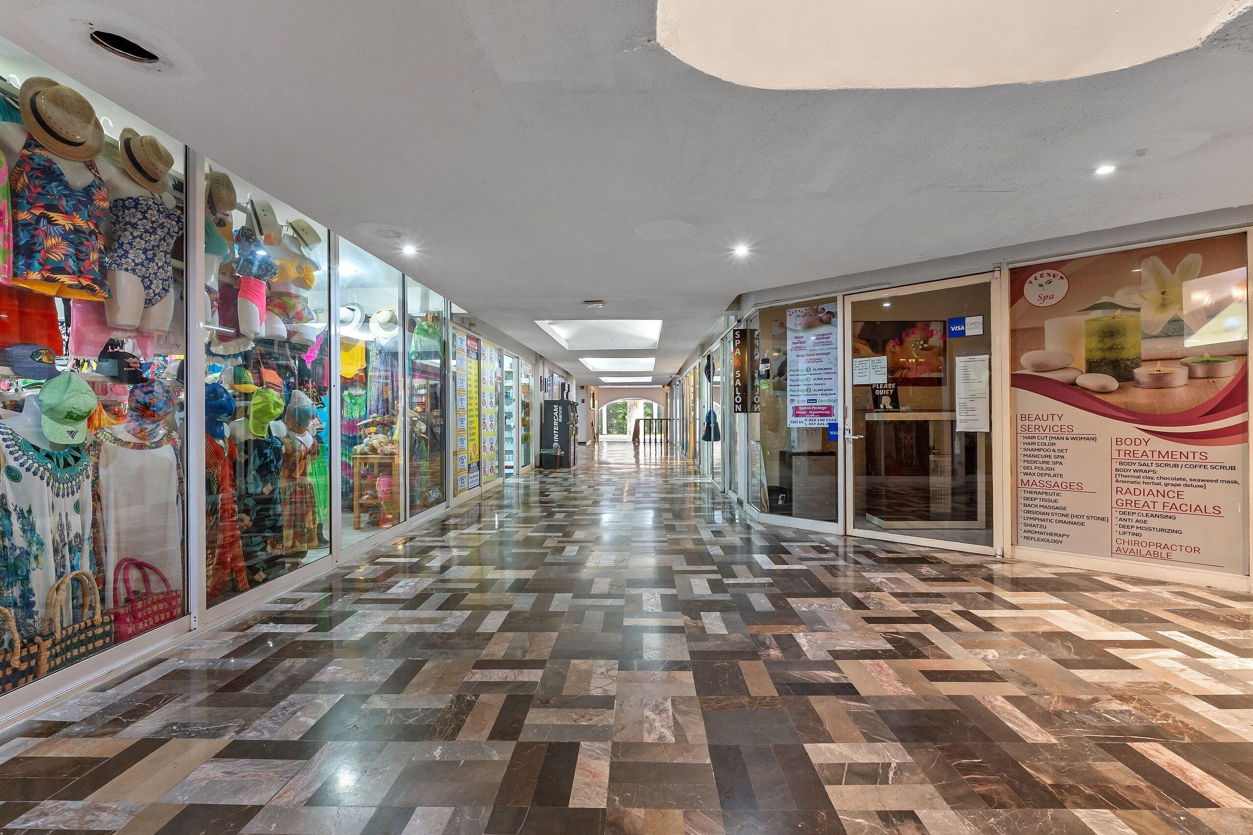 A corridor with glass storefronts on both sides, a tiled floor, and a ceiling with recessed lighting.