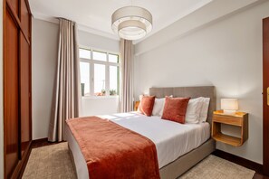 Ein Hotelzimmer mit Bett, Nachttisch, Fenster mit Vorhängen und Deckenleuchte.