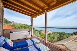 A balcony with a wooden ceiling, a white bathtub, and blue striped cushions.