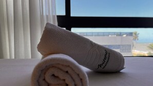 A rolled towel and a pillow on a bed with a view of a bridge and palm trees through a window. - Setai Aquamares - Miramar Hospedagens (João Pessoa)