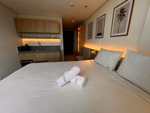 Una habitación de hotel con cama, una kitchenette pequeña, un baño y un pasillo.