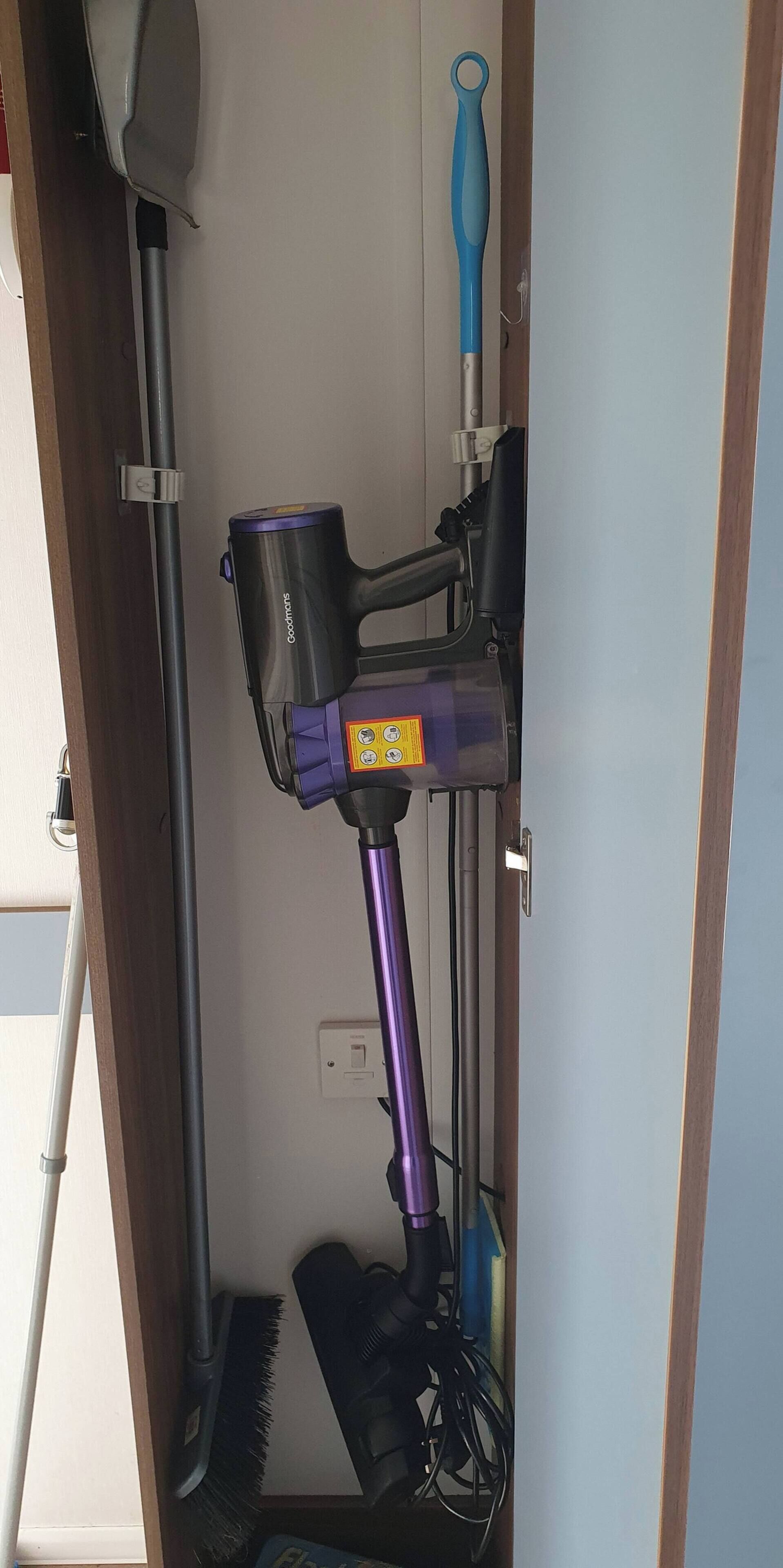 Un aspirateur, un balai et un outil  à manche bleue dans une pièce aux murs en bois et au plafond blanc.
