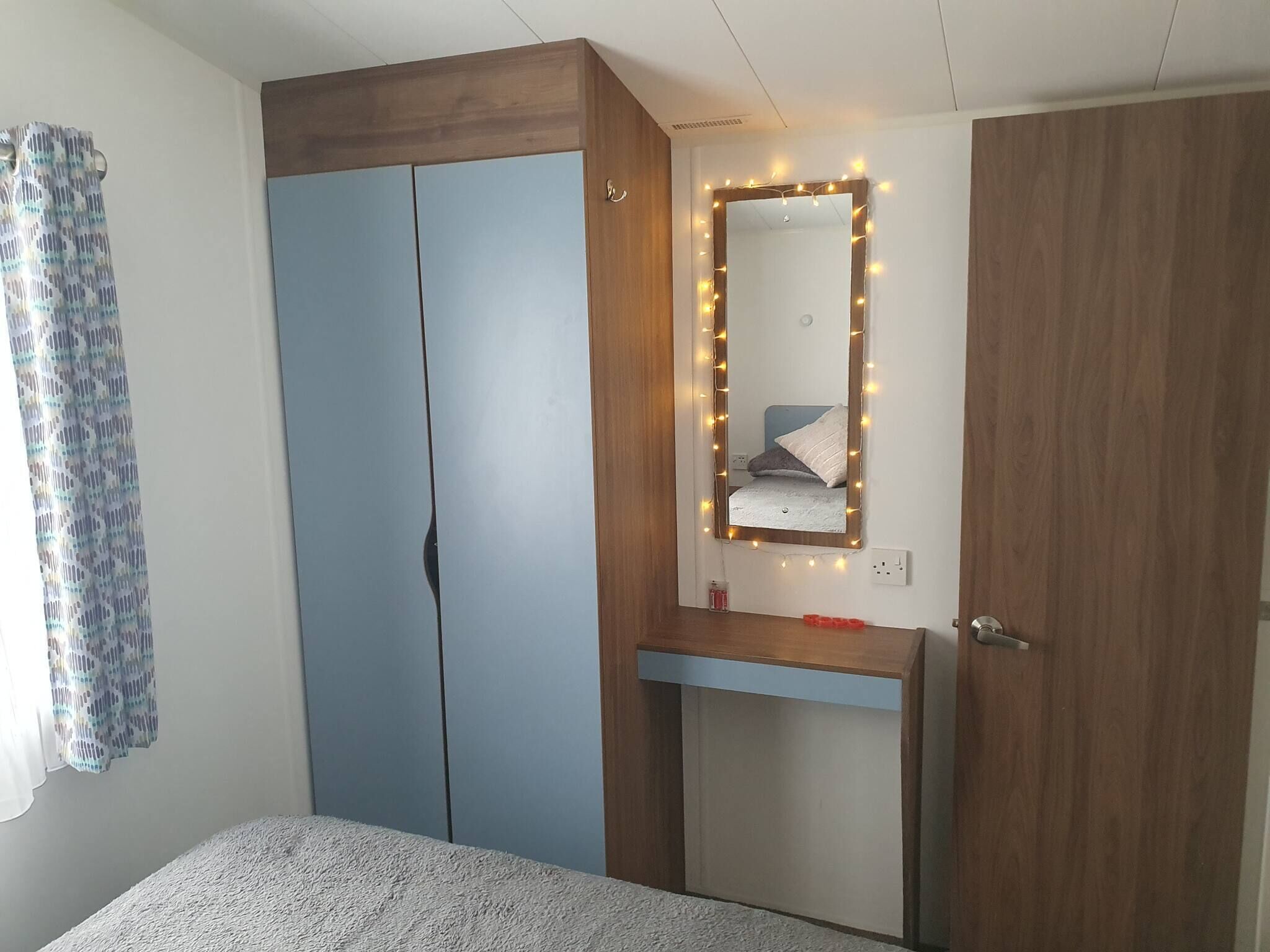 Een slaapkamer met een garderobe, nachtkastje en een spiegel met verlichting.