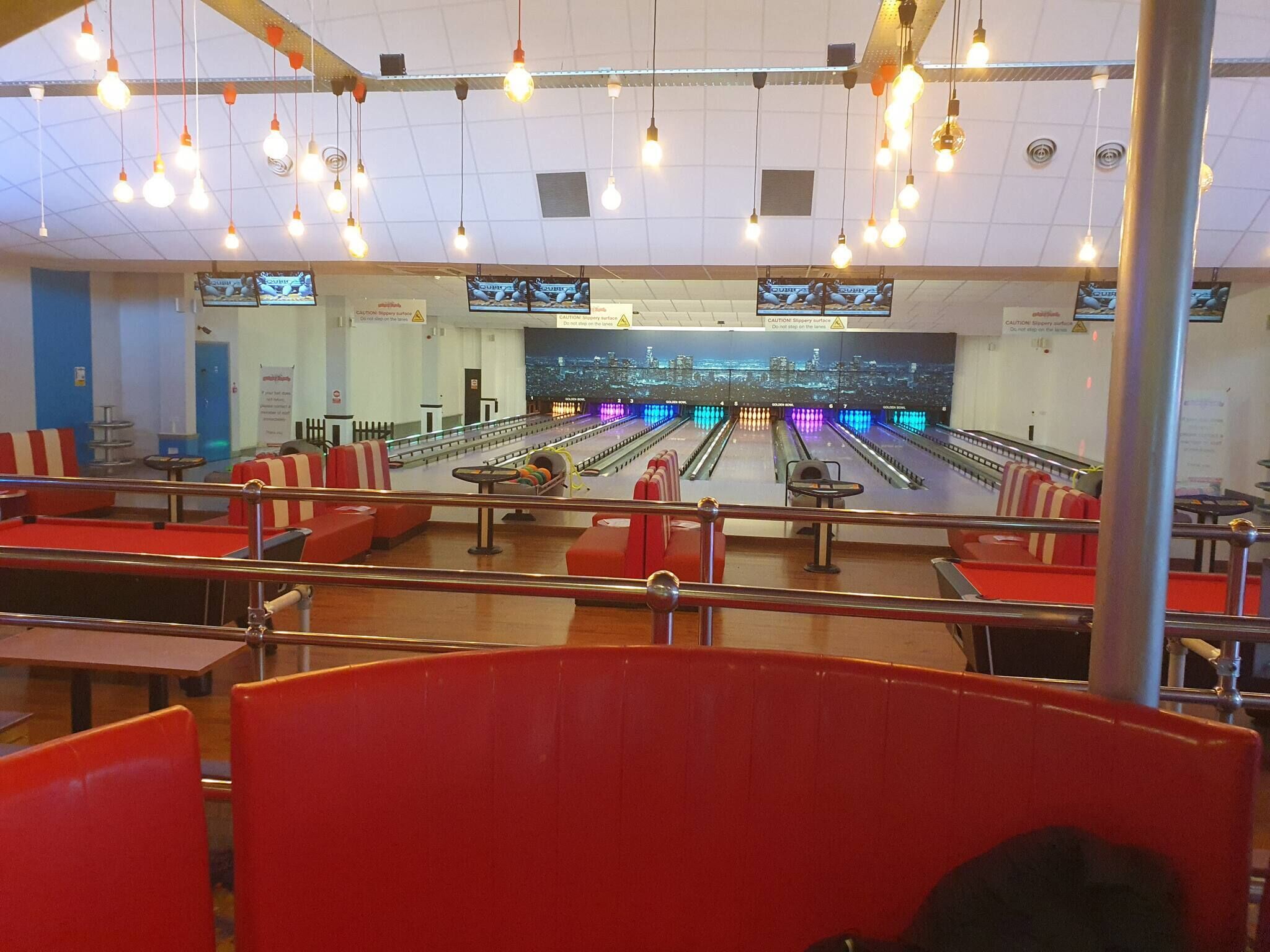 Un bowling doté de nombreuses pistes, de sièges rouges, d’un éclairage suspendu et offrant une vue sur le paysage urbain.