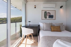 Ein modernes Schlafzimmer mit Bett, Nachttisch, Stuhl und Blick auf die Stadt.