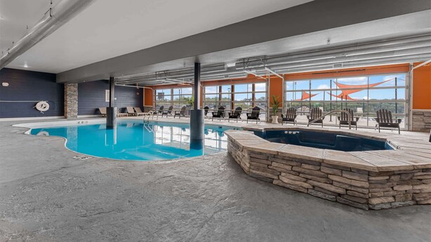 Piscina interna con sedie a sdraio e vasca idromassaggio, ampie finestre e una parete in pietra.