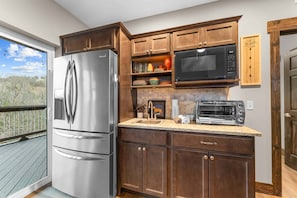 A kitchen with a stainless steel refrigerator, a microwave, a toaster, and wooden cabinets. - Kokomo Kove Hot Tub, Views (Branson)