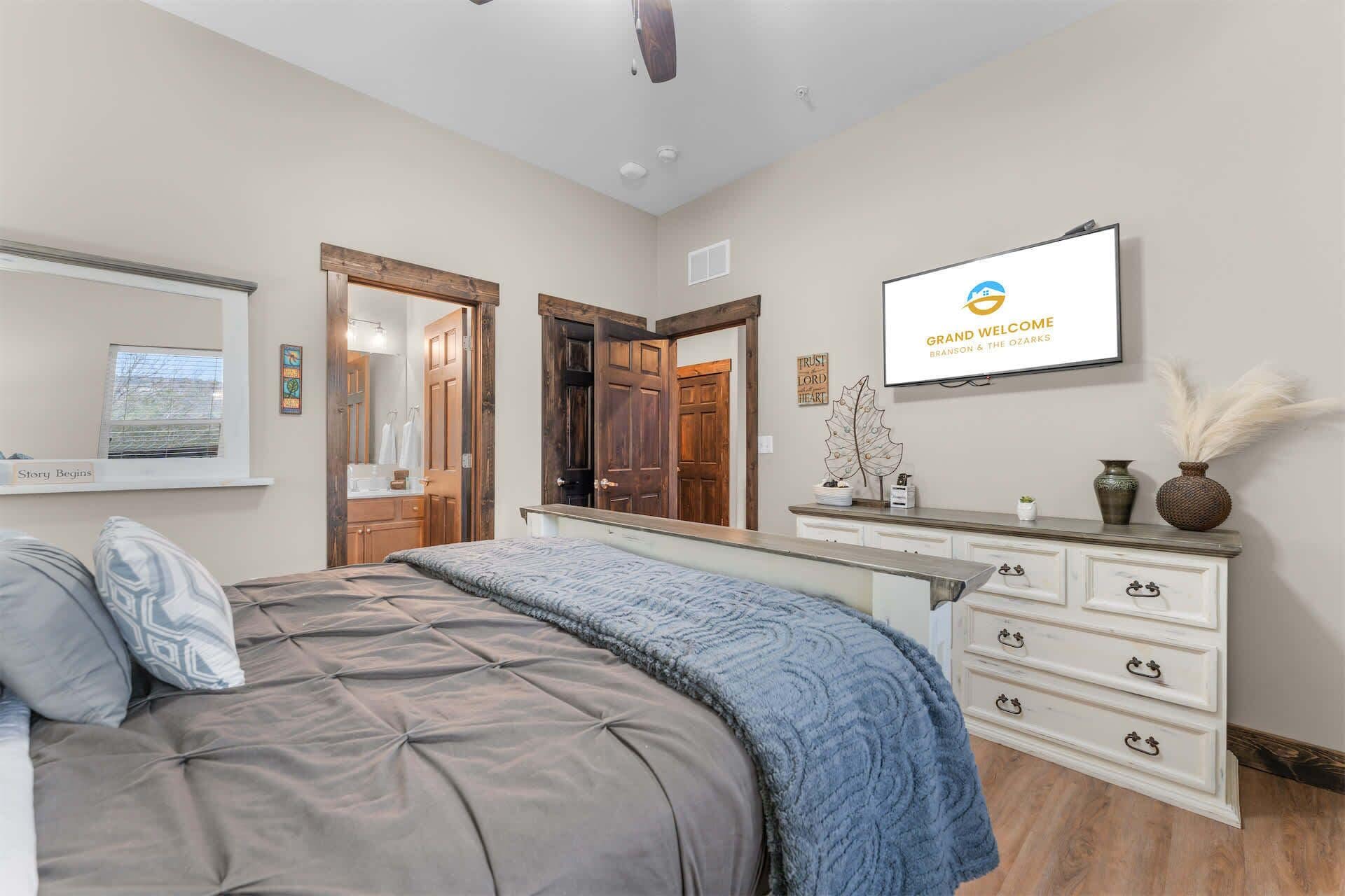 A bedroom with a bed, dresser, TV, and a door leading to another room.