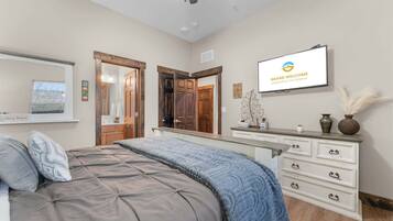 A bedroom with a bed, dresser, TV, and a door leading to another room.