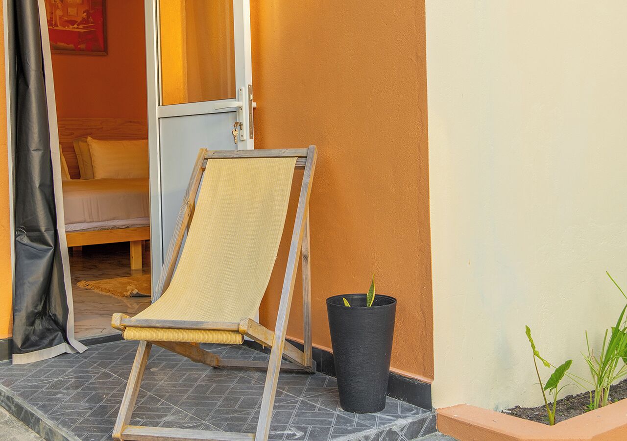 A room with a bed, a chair, a potted plant, and a door.