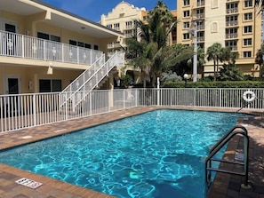 A swimming pool with a white railing and a no diving sign, surrounded by a building with balconies and palm trees.
