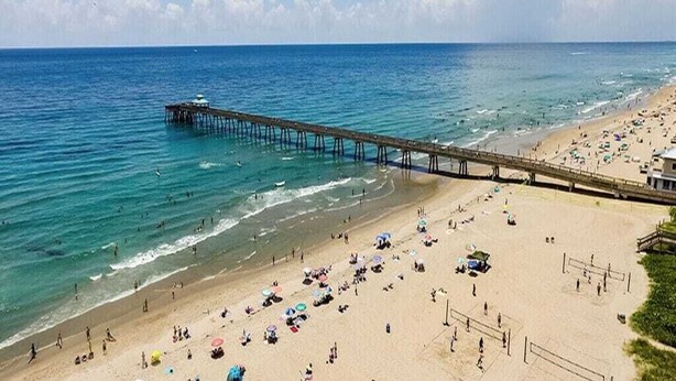 Uma praia com um píer que se estende para o oceano, areia e guarda-sóis.