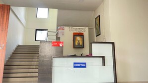 Zona d'entrada amb una escala, una taula de recepció, un quadre amb marc i un rellotge penjat a la paret.