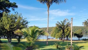 A serene outdoor area with a grassy lawn, palm trees, and a body of water in the background. - Guesthouse facing Silves, 5 minutes from the bus terminal, with river access. (Silves)