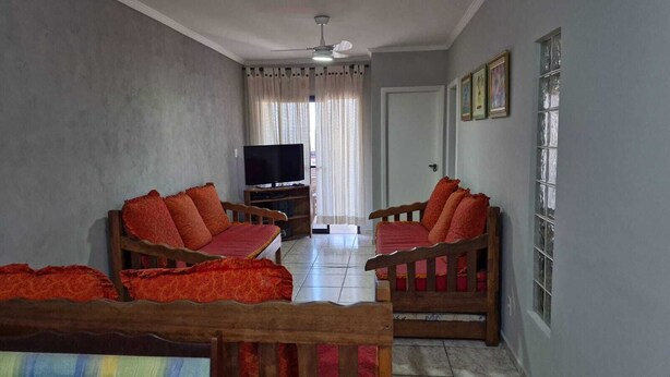 A living room with two wooden sofas, a television, and a window with curtains. - APARTMENT IN PRAIA GRANDE – VILA TUPI | COMFORT, LOCATION AND INCREDIBLE VIEW (Praia Grande)