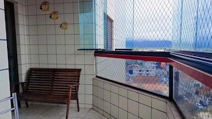 A balcony with a wooden bench, tiled walls, and a view of a parking area through a chain-link fence. - APARTMENT IN PRAIA GRANDE – VILA TUPI | COMFORT, LOCATION AND INCREDIBLE VIEW (Praia Grande)
