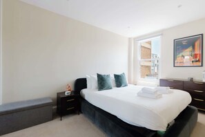 A hotel room with a bed, a nightstand, a dresser, and a window with a view of buildings. - Gorgeous 1BDR Flat in the Heart of Clapham (Greater London)