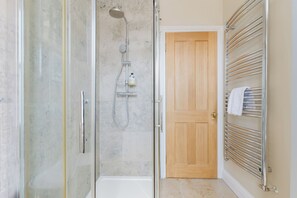 A bathroom with a glass-enclosed shower, a wooden door, and a towel rack with towels. - Gorgeous 1BDR Flat in the Heart of Clapham (Greater London)