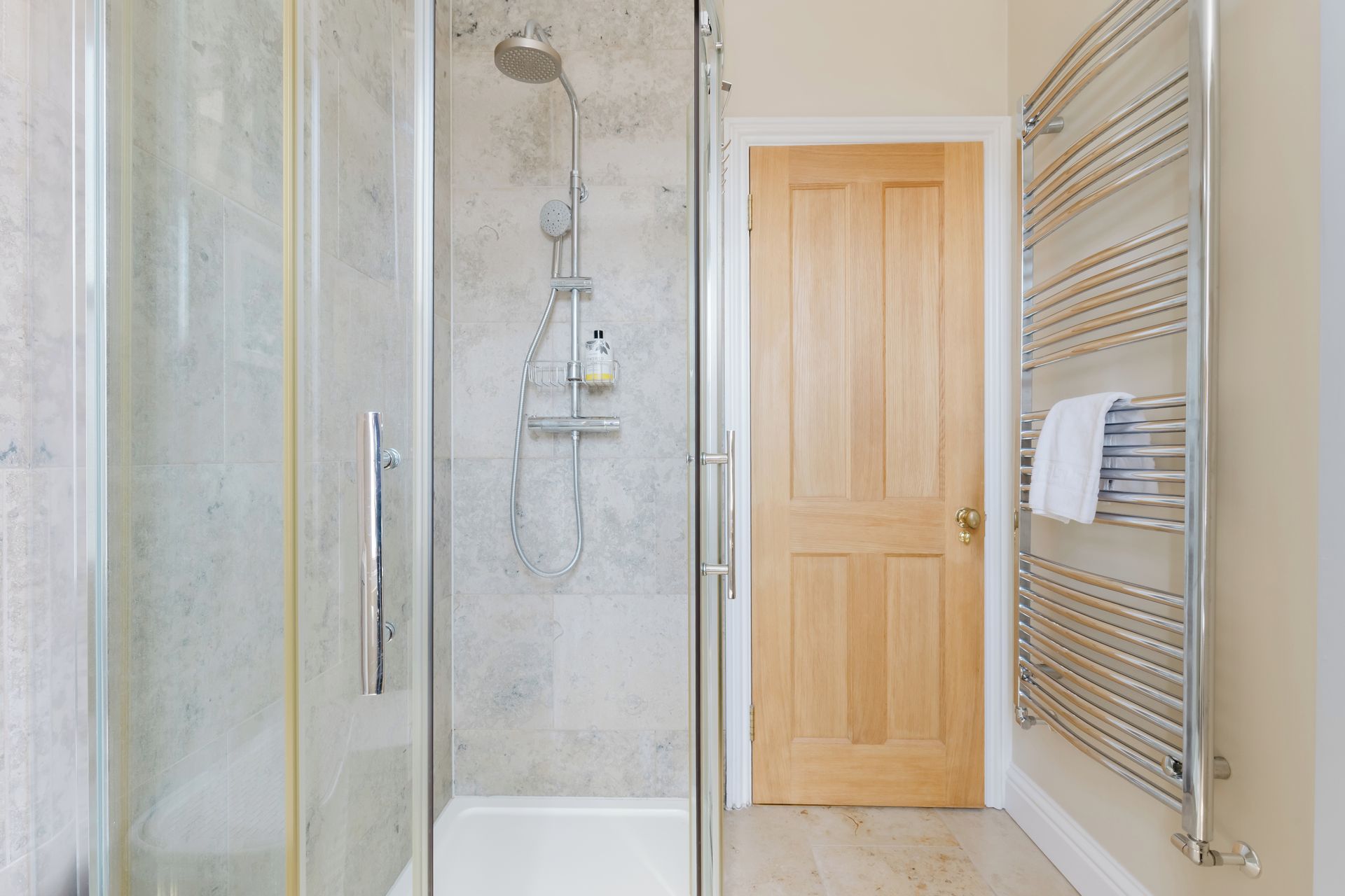 A bathroom with a glass-enclosed shower, a wooden door, and a towel rack with towels.