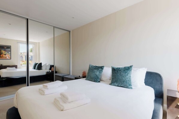 A hotel room with a large bed, a bedside table, a mirror, and a view of the outside. - Gorgeous 1BDR Flat in the Heart of Clapham (Greater London)