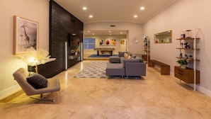 A modern living room with a sectional sofa, a chair, a coffee table, and a fireplace. There is a dining area in the background with a dining table and chairs. - Villa Azur by Glam Homes (North Miami Beach)